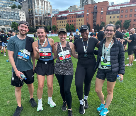 Five team members posing together with race bibs after completing a road race