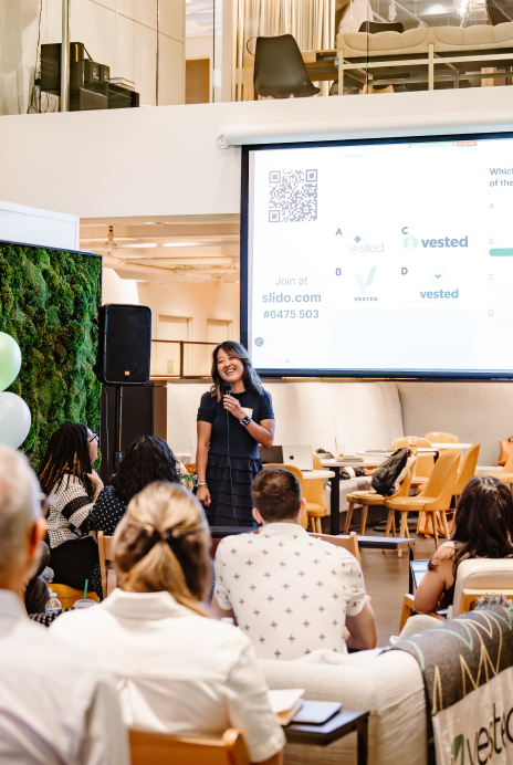 Team member presenting to colleagues at a Vested company meeting with a projected slide visible in the background